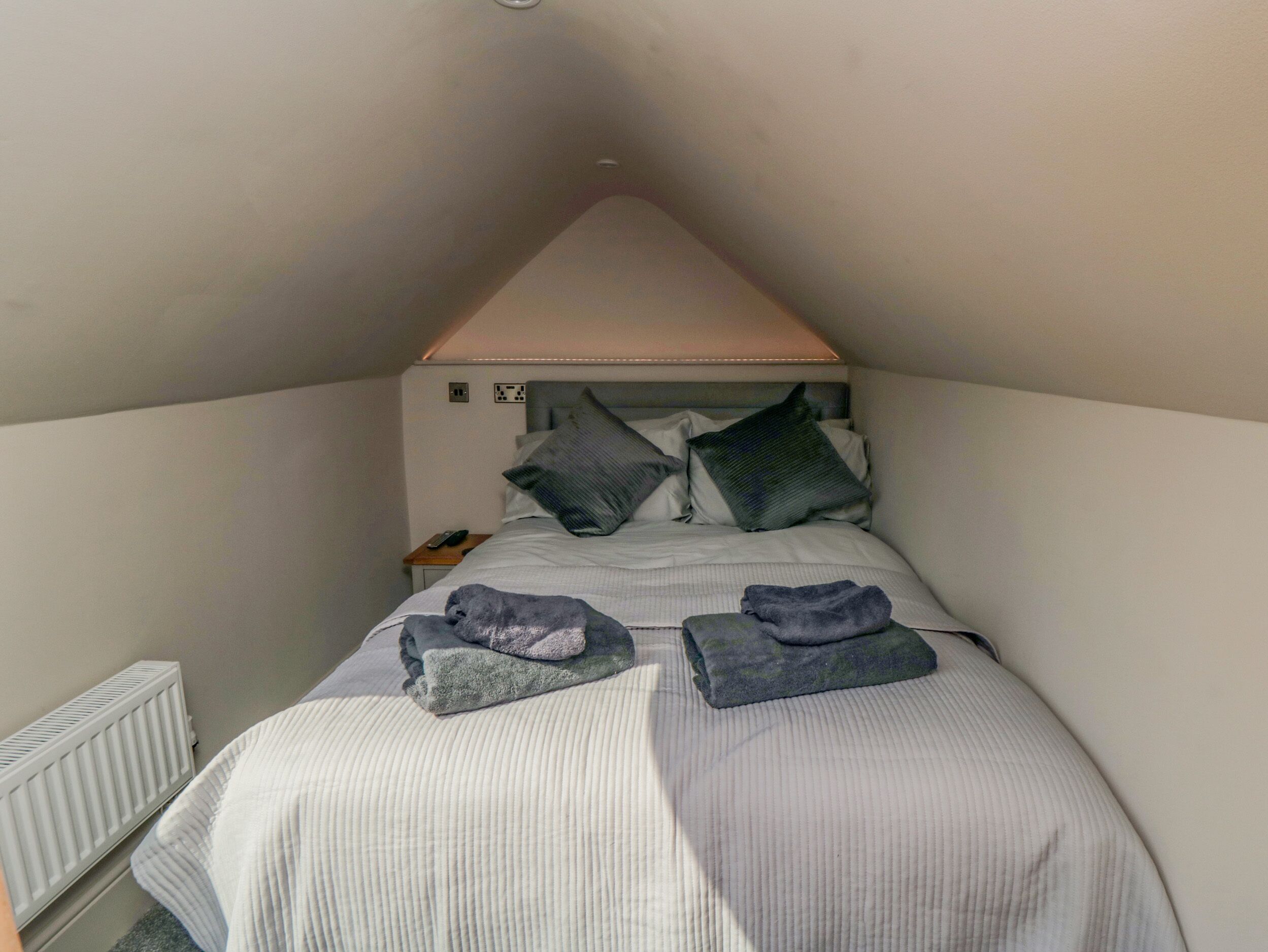 A small, triangular room with a bed, pillows, a nightstand, and a radiator.
