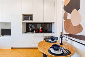 Een moderne keuken met witte kastjes, een magnetron en een fles wijn op een houten tafel.