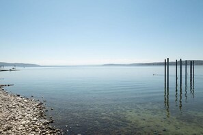 Ein ruhiger See mit steiniger Uferlinie und einem Steg, der ins Wasser führt.