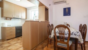 A kitchen with wooden cabinets, a dining table with chairs, and an air conditioning unit on the wall. - Natasas Apartments (Zakynthos)