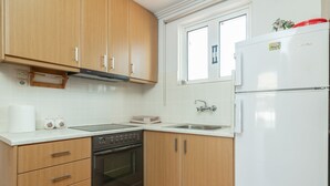 A kitchen with wooden cabinets, a built-in oven, a sink, and a white refrigerator. - Natasas Apartments (Zakynthos)