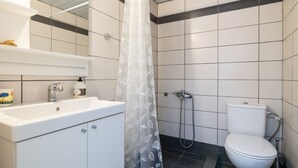 A bathroom with a white sink, a toilet, and a shower with a transparent curtain. - Natasas Apartments (Zakynthos)