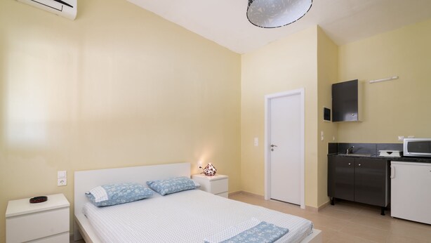 A bedroom with a bed, nightstand, and a small kitchenette area. - Natasas Apartments (Zakynthos)