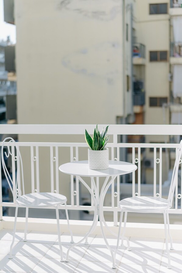 A balcony with a round table and two white chairs, a potted plant, and a white railing.