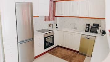A compact kitchen with white cabinets, a stainless steel refrigerator, a black oven, a microwave, and a dishwasher.