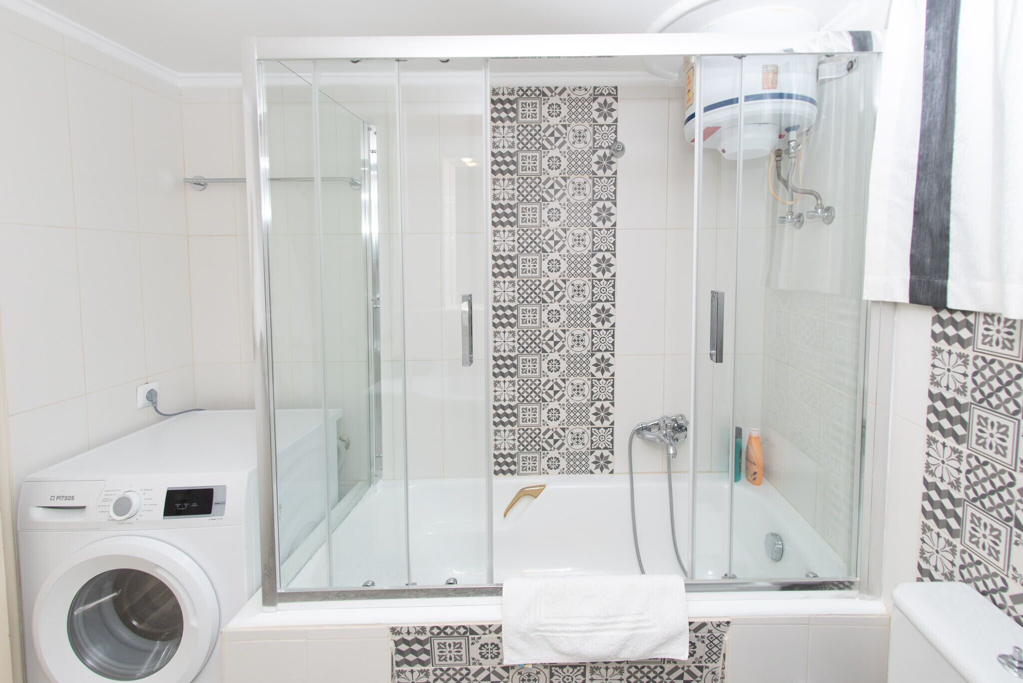 Un baño moderno con ducha envuelta en vidrio, lavadora integrada y azulejos estampados.