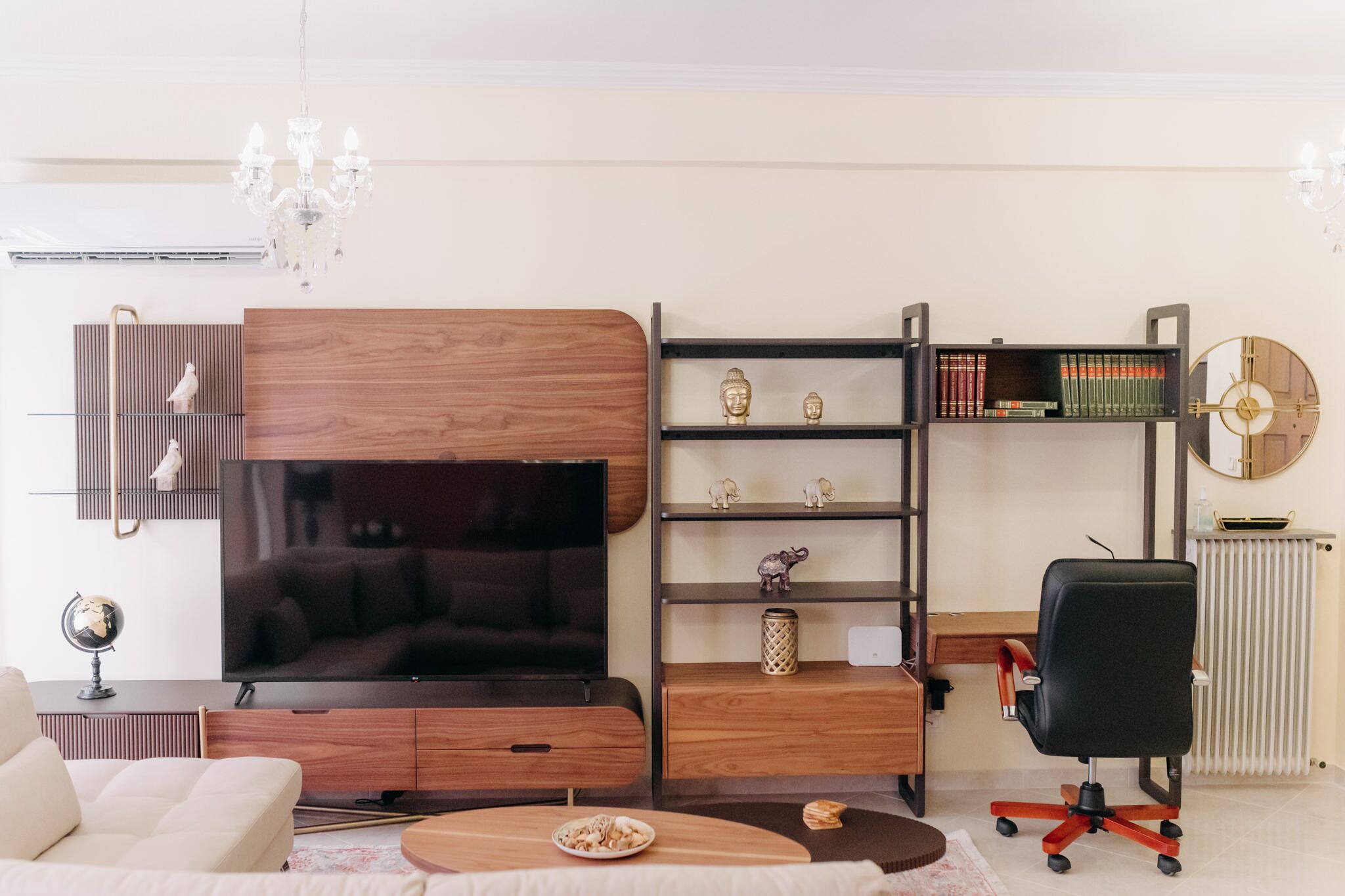 Een moderne woonkamer met een flatscreen televisie, houten meubels, een boekenkast en een bureau met stoel.