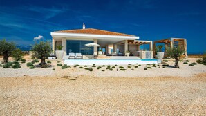 Una casa moderna con piscina, mobiliario exterior y vistas al mar.