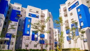 Un moderno edificio residenziale con facciate blu e bianche, piani numerati e un giardino curato.