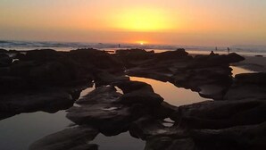 Tramonto su una costa rocciosa con acque calme che riflettono il cielo.