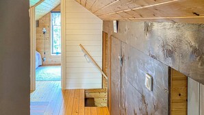 Ein Holzinnenraum mit einer Treppe, die zu einer zweiten Etage führt, einer Tür mit Griff und einem Fenster, das natürliches Licht hereinlässt.