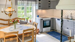 Eine Küche mit einem weißen Backofen, einer Spülmaschine und einem Waschbecken. Es gibt einen Tisch mit Stühlen und eine Vase mit Blumen.