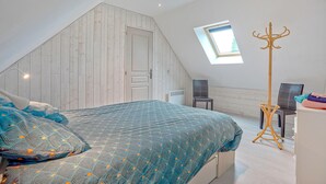 Ein Schlafzimmer mit schrägen Wänden, einem Oberlicht, einem Bett mit gemusterten Textilien, einem Kleiderständer und einem Sessel.