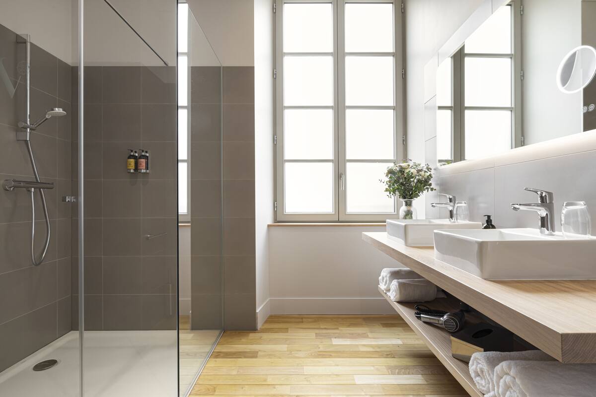 A modern bathroom with a glass shower enclosure, a large window, and a vanity with a mirror.