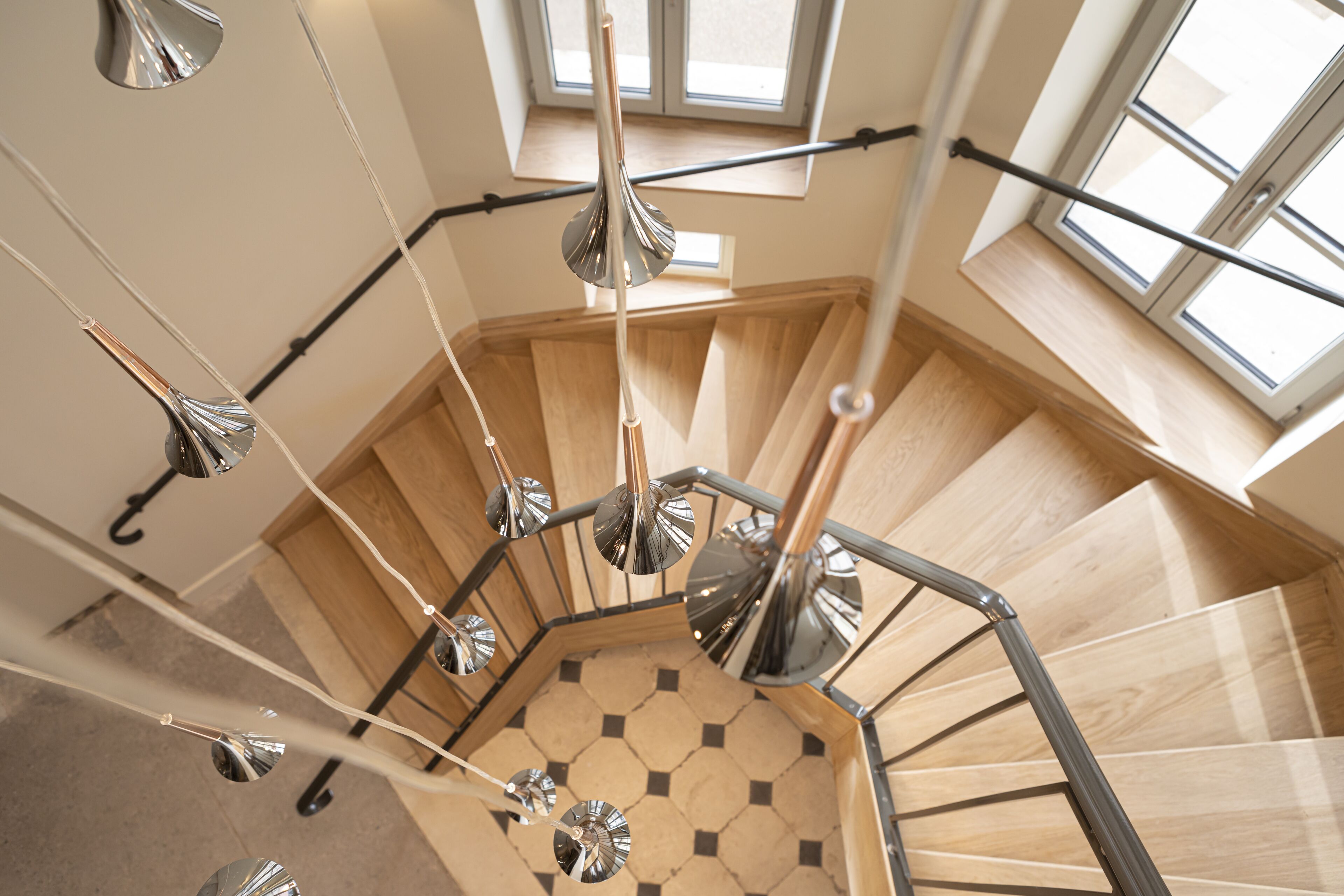 Un escalier en colimaçon avec des marches en bois et un sol orné d’un motif géométrique.
