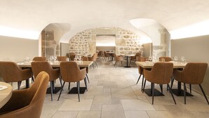 A restaurant with stone walls, round tables, and brown chairs.