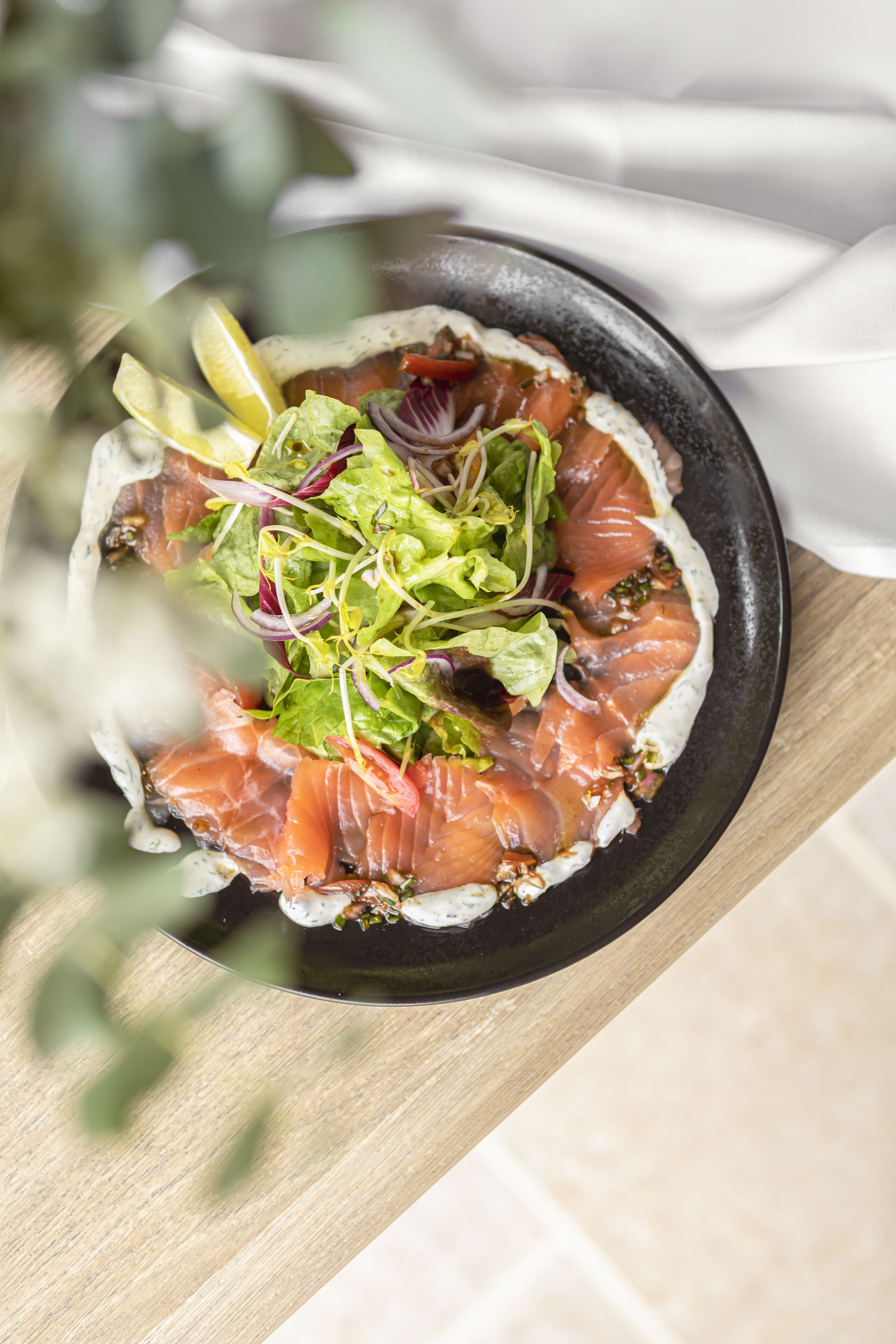 A bowl of smoked salmon with greens on a wooden table.
