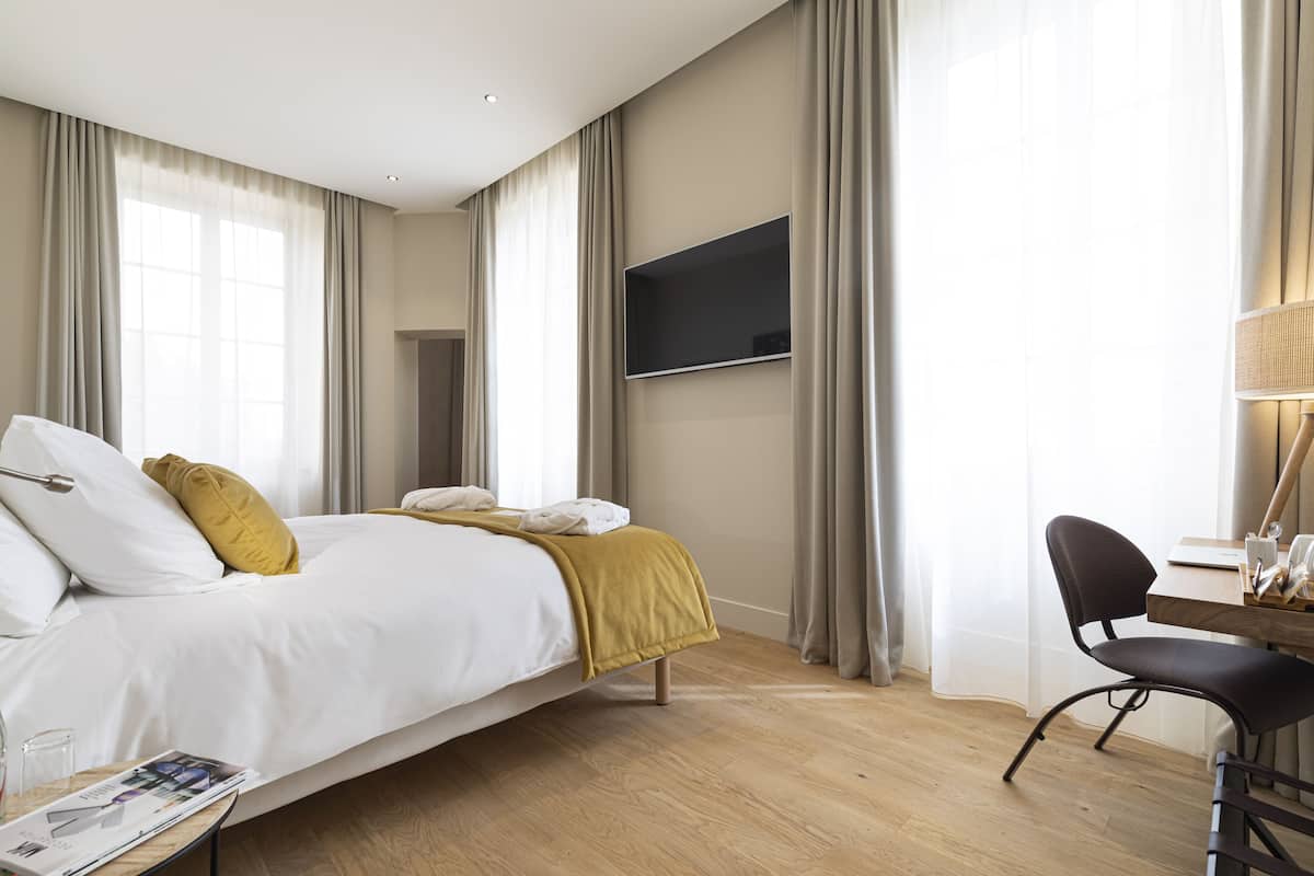 A hotel room with a bed, a desk, a chair, a TV, and curtains.
