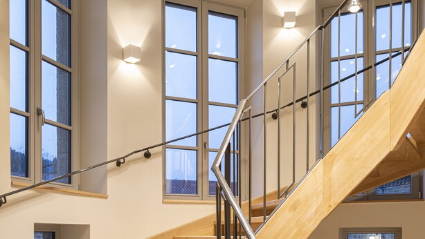 A modern staircase with wooden steps and metal railings, leading to a second floor with large windows and hanging pendant lights.