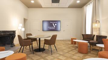 A modern hotel room with a fireplace, a TV screen displaying a welcome message, and a seating area with ottomans and chairs.