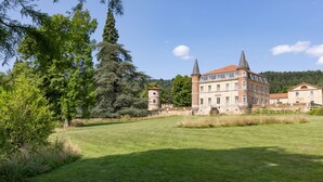 A large, historic building with two prominent towers, surrounded by lush greenery and a well-maintained lawn.