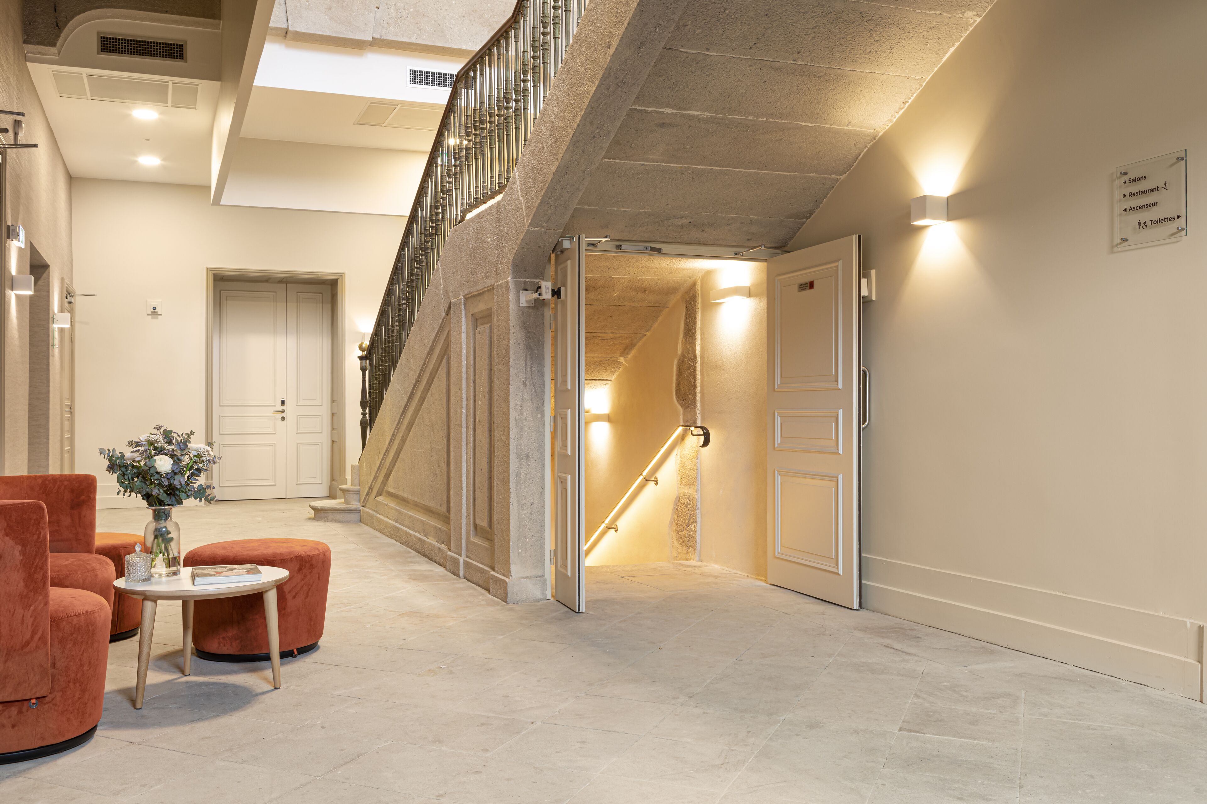 Eine Hotelhalle mit Treppe, einer Rezeption und einer Sitzecke mit Blumenvase.