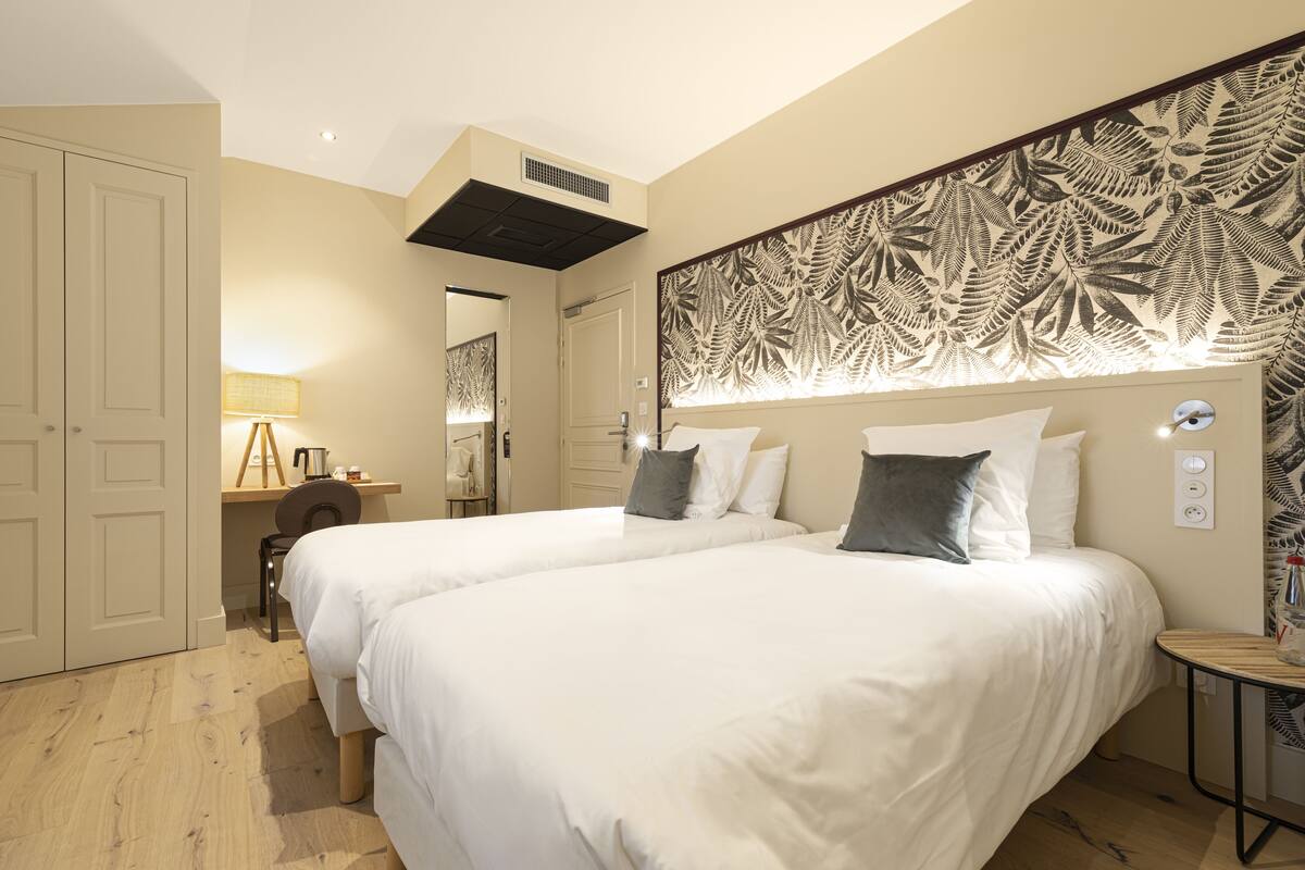 A hotel room with two beds, a desk with a lamp, and a decorative headboard.