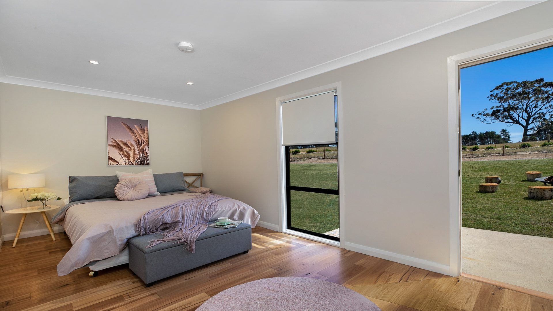 A bedroom with a bed, bedside table, and a view of a grassy outdoor area through a sliding door.