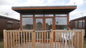 Une terrasse en bois dotée d’une enceinte en verre, d’une porte métallique et d’une petite marche menant à la terrasse.