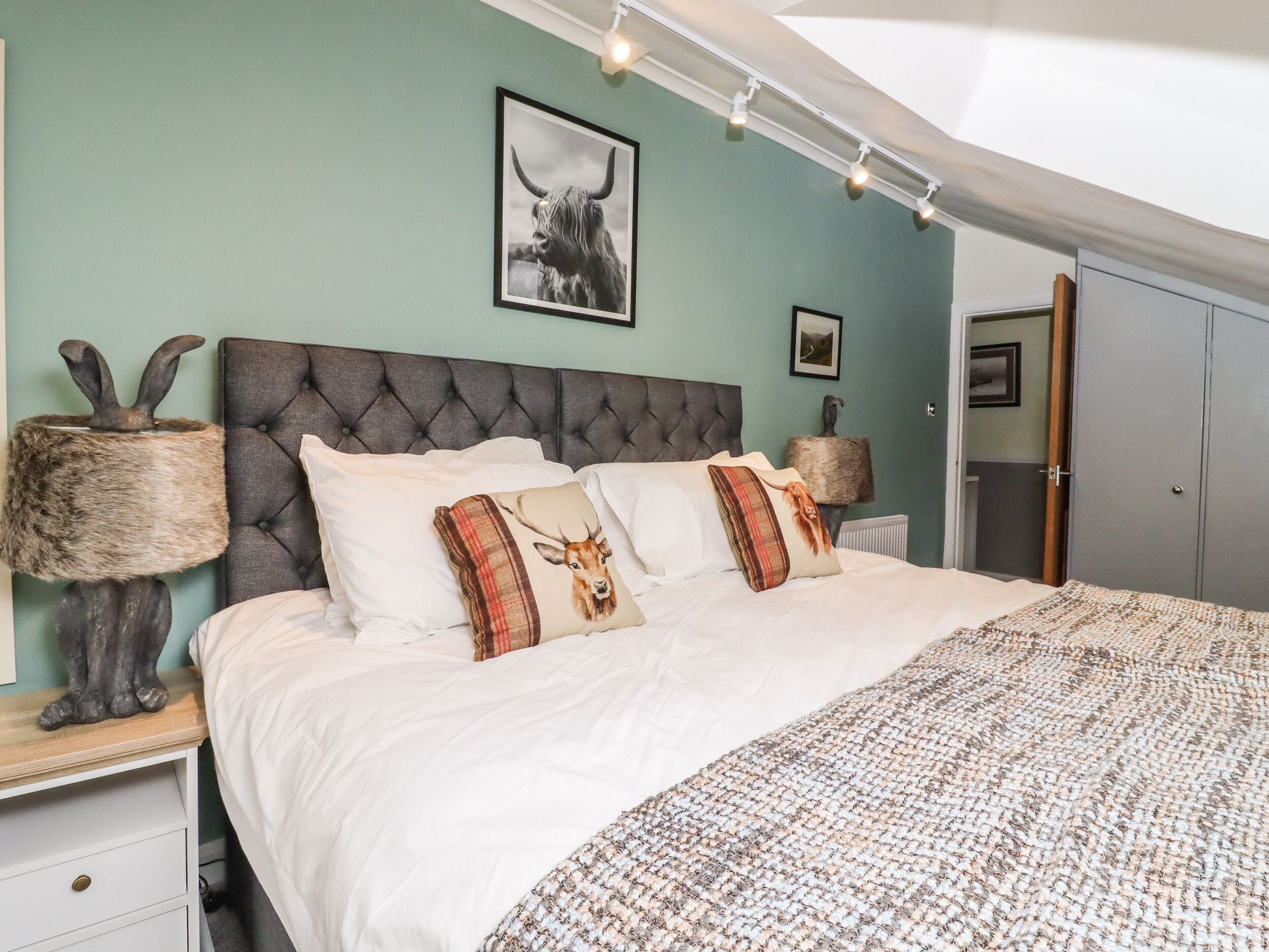 Une chambre à coucher avec une tête de lit capitonnée, un couvre-lit blanc et des coussins décoratifs ornés de motifs animaliers.