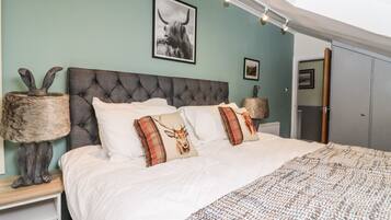 Une chambre à coucher avec une tête de lit capitonnée, un couvre-lit blanc et des coussins décoratifs ornés de motifs animaliers.