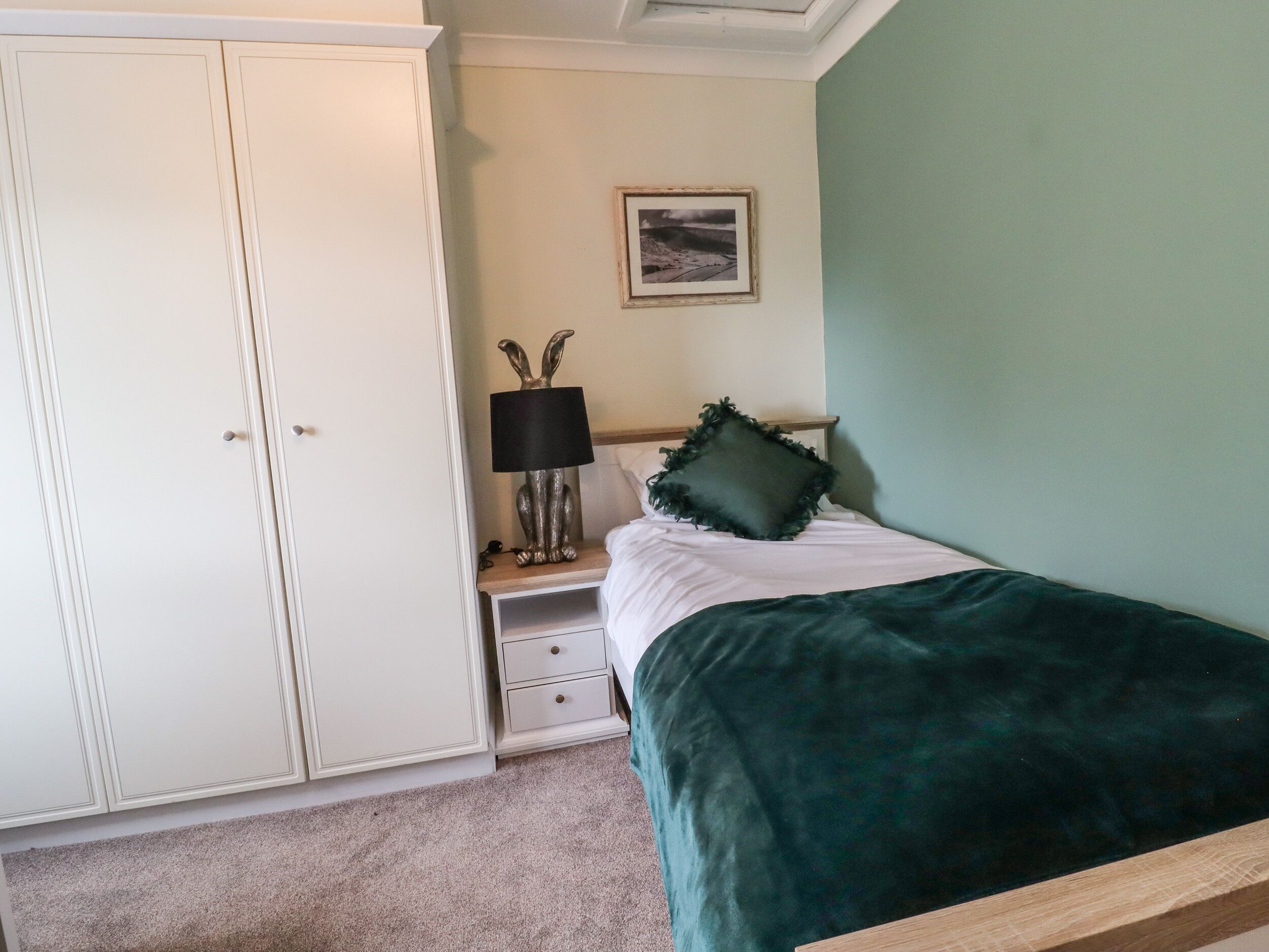 A bedroom with a bed, a nightstand, a lamp, a picture on the wall, and a wardrobe.