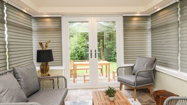 A modern living room with a sofa, armchairs, a coffee table, and a lamp. There is a sliding glass door leading to an outdoor patio with a table and chairs. - Bowland Fell Cottage (Skipton)