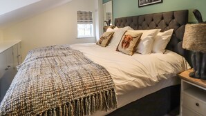 A bedroom with a large bed, a tufted headboard, and a window with blinds. - Bowland Fell Cottage (Skipton)