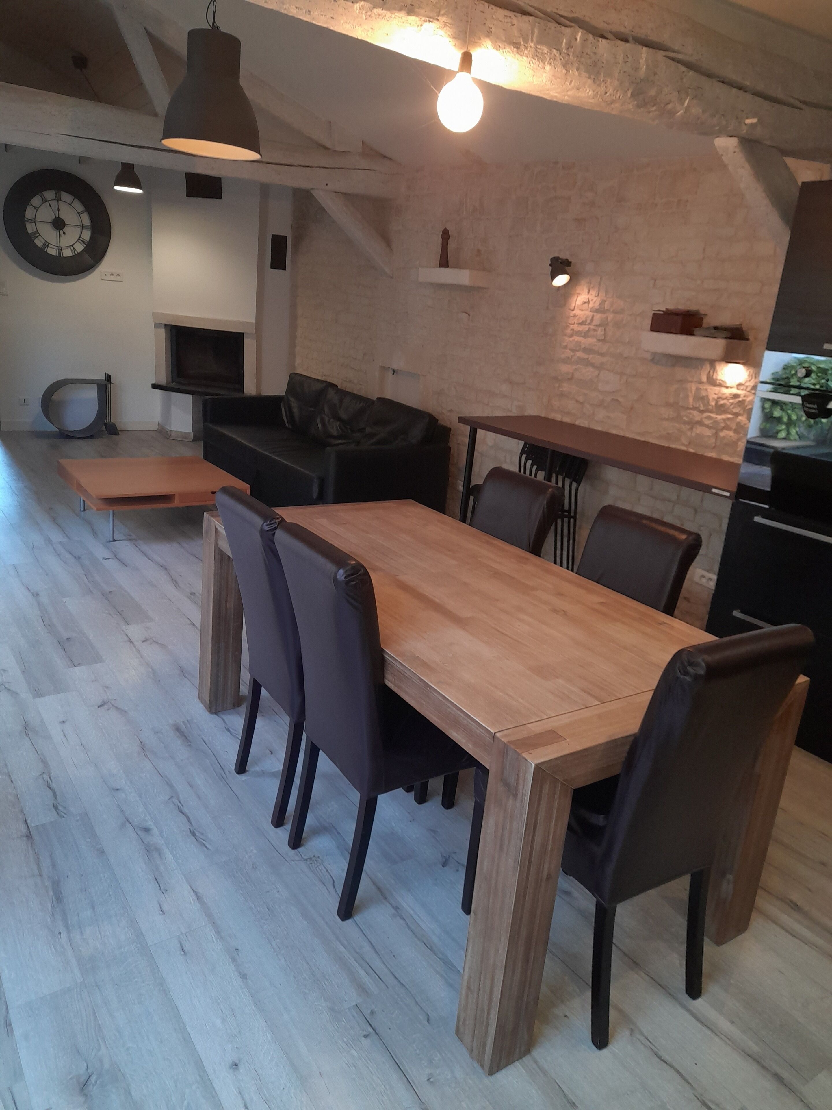 A modern kitchen with a wooden dining table and chairs, a black leather sofa, and a stone wall.