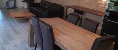 A modern kitchen with a wooden dining table and chairs, a black leather sofa, and a stone wall.