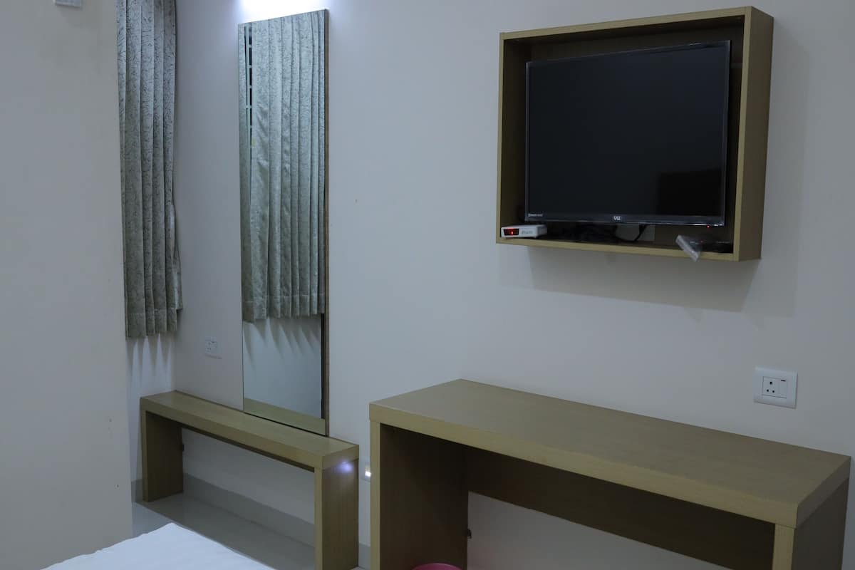 A bedroom with a bed, a wooden desk, a television, and a mirror.