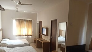 A hotel room with two beds, a TV, a desk, a mirror, and a ceiling fan. - KRV Meridian (Modakurichi)