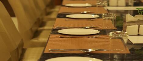 A long dining table set with plates, cutlery, and glasses, flanked by chairs.