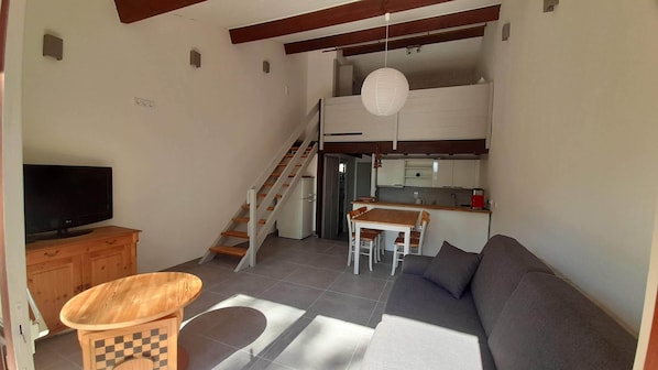 Uma sala de estar com sofá, mesa de madeira, televisão e escada que leva a uma cozinha.