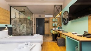 A hotel room with two beds, a desk with a computer, a TV, and a bathroom with a shower and mirror. - Urban Hotel (Plovdiv)