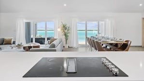 A modern hotel room with a dining area, large windows with a view of the ocean, and a central table with chairs. - Private Beachfront Luxury Villas with Dock & Heated Pools – Perfect for 10 Guests (Exuma)