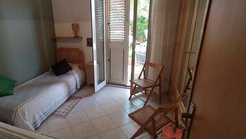 Un dormitorio con una cama, una silla, una mesita y una puerta que da a un espacio exterior.