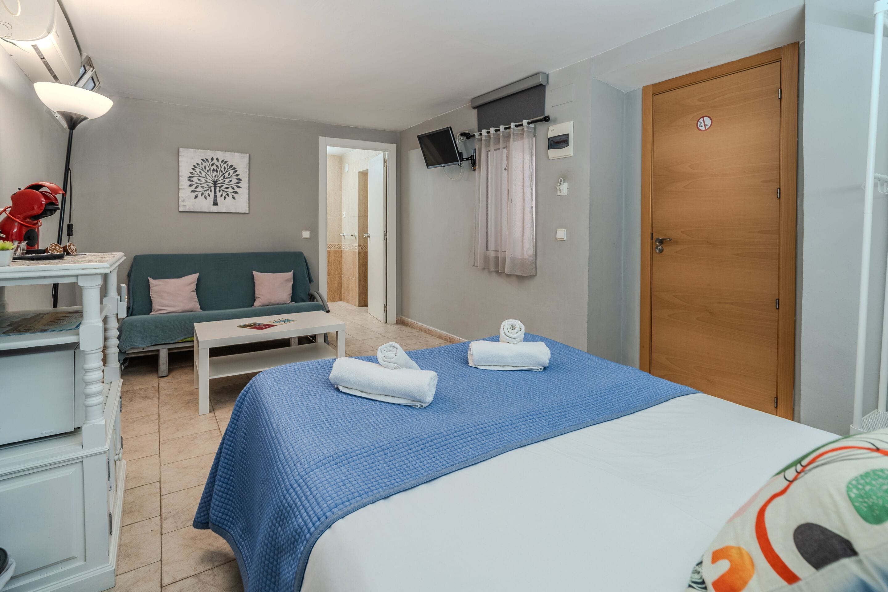 Une chambre d’hôtel avec un lit, un canapé, un téléviseur fixé au mur et une porte en bois.