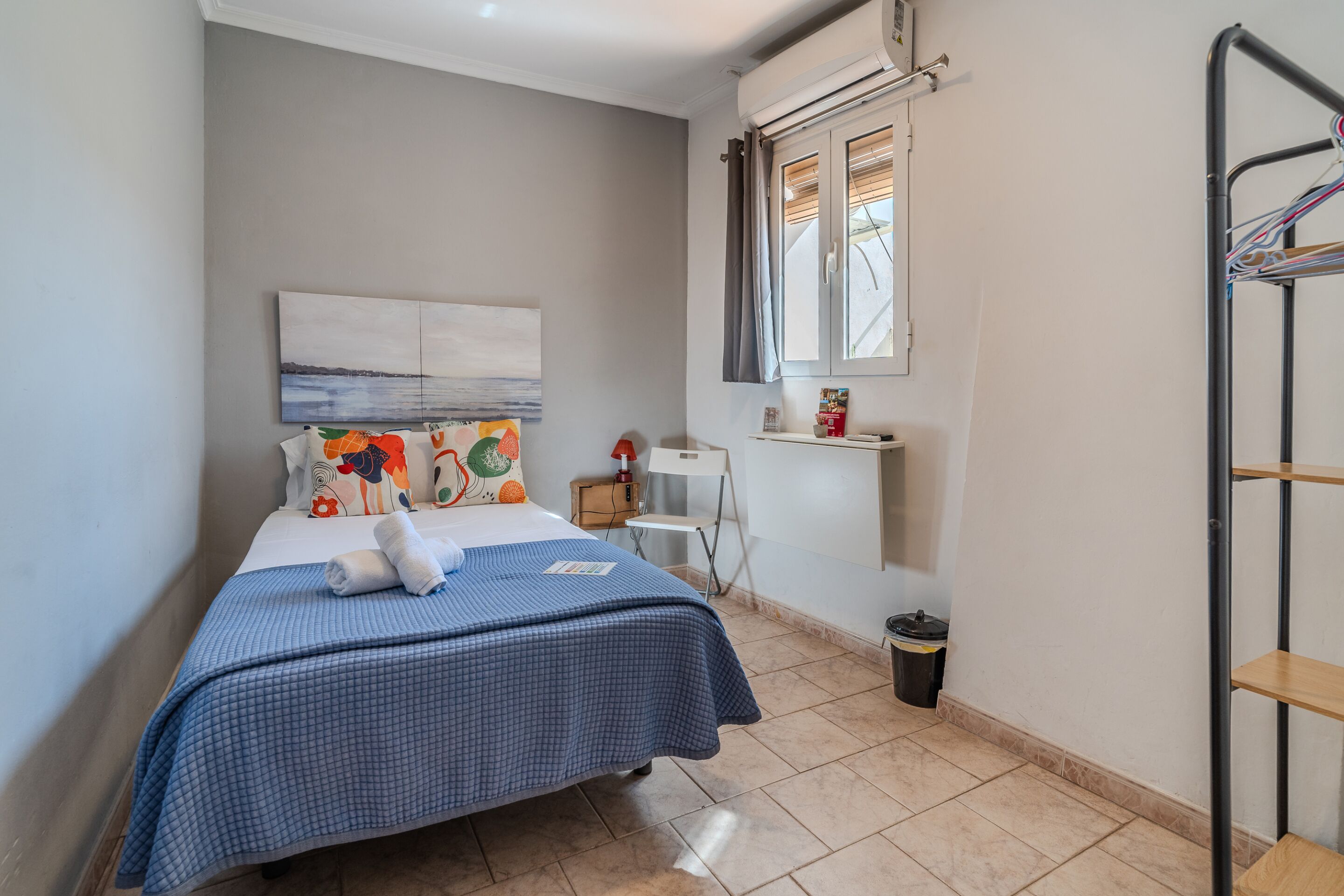 Une chambre à coucher avec un lit, une fenêtre avec des rideaux, un petit bureau et une chaise.