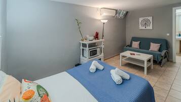Une chambre d’hôtel avec un lit, une petite table blanche, un canapé, un four à micro-ondes et un climatiseur fixé au mur.