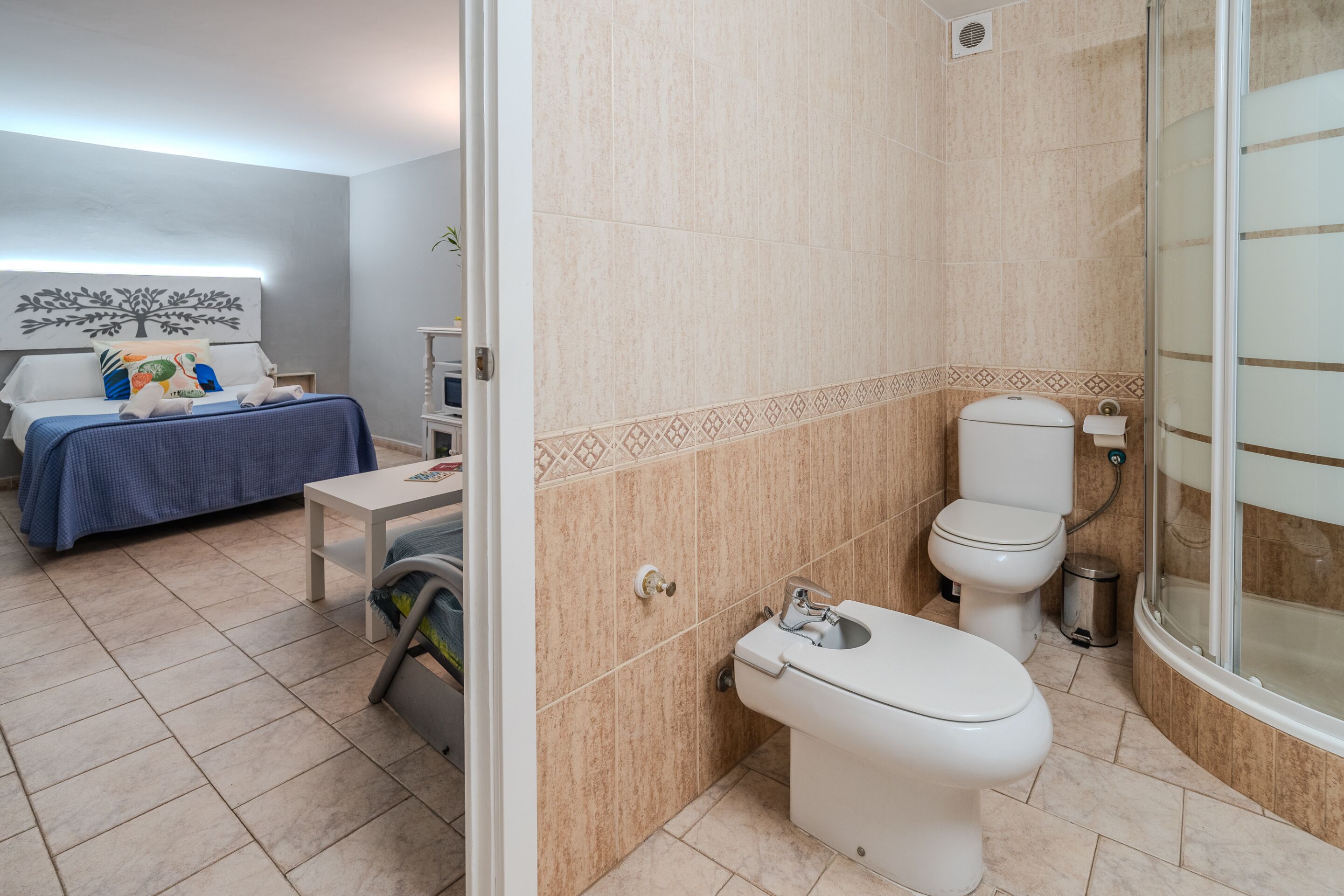 Un dormitorio con cama, mesita de noche y baño completo con inodoro, lavamanos y ducha.