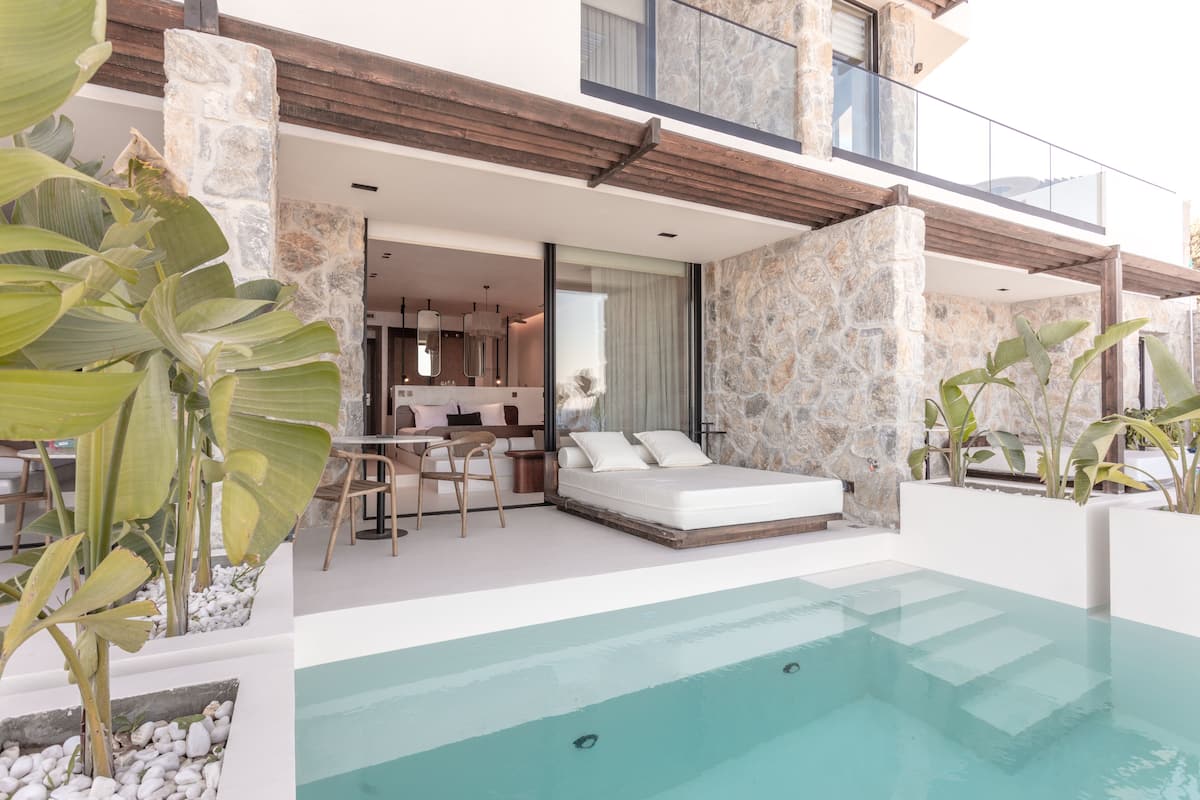 A modern outdoor pool area with a stone wall, a sofa, and a dining area with a table and chairs.