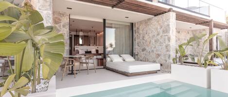 A modern outdoor pool area with a stone wall, a sofa, and a dining area with a table and chairs.
