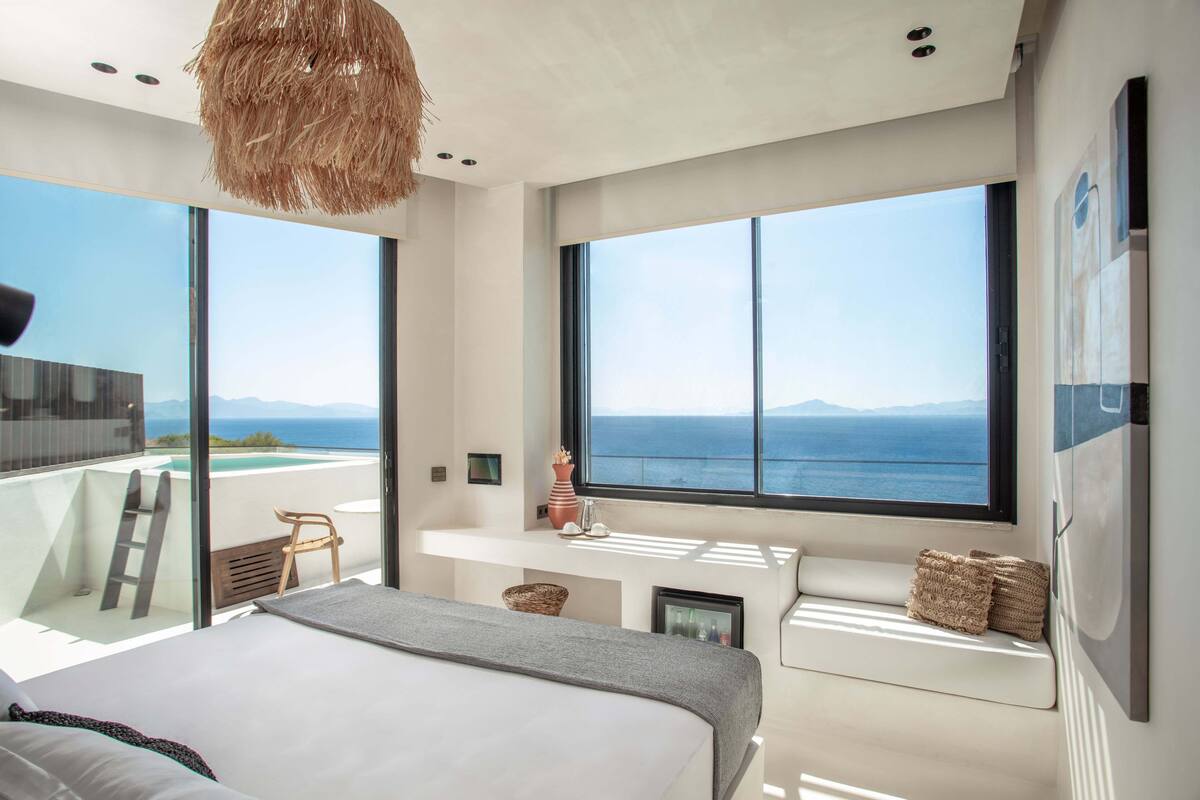 A modern bedroom with a large bed, a small desk, and a view of the ocean.